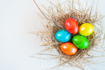 Multi-colored Easter eggs lie in a straw, as in a nest.