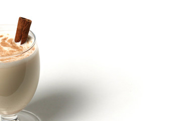 Eggnog Christmas cocktail in a transparent wine glass, decorated with cinnamon stick, sprinkled with grated nutmeg. Isolated on white background. Copy space.