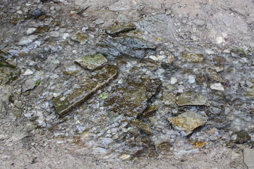 Background, texture with a small transparent stream flowing on the ground with flat small stones.