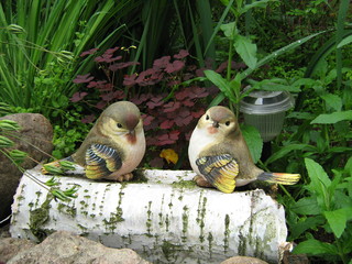 Still life with two toy birds Tits on a birch log near a large stone, grass and a night lamp.