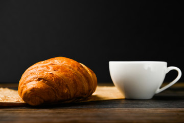 coffee with croissant on a dark background. the beginning of the morning. A cup of coffee. fresh french croissant. Coffee cup and fresh baked croissants on a wooden background. View from above.