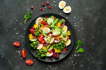 Salad with pomegranate, eggs, tomatoes, fresh cucumbers, onions, sesame and bell pepper, spices on a stone background. Healthly food.
