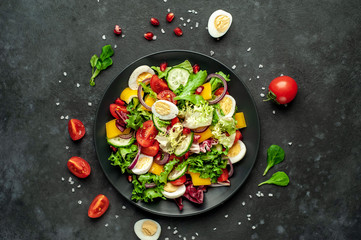 Salad with pomegranate, eggs, tomatoes, fresh cucumbers, onions, sesame and bell pepper, spices on a stone background. Healthly food.