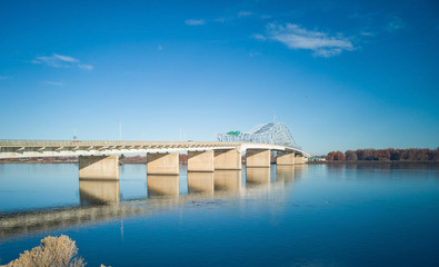 Historic blue and white arch truss bridge over the Columbia River with blue skies and clouds on a sunny morning in Kennewick-Pasco Washington