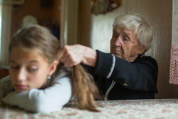 Elderly woman braids her granddaughter's hair.