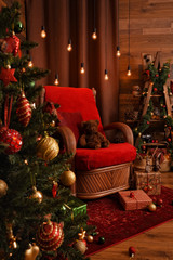 Modern cozy interior in red and brown shades with an armchair and decorated Christmas tree. Teddy bear sitting on the chair, gifts, garlands and other Christmas decorations. 