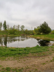 A lake in a city Park with reflected lanterns and gray clouds surrounded by young green grass and sparse trees