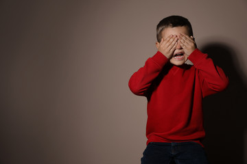 Scared little boy on beige background, space for text. Domestic violence concept
