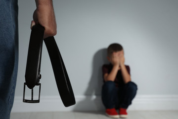 Man threatening his son with belt indoors, closeup. Domestic violence concept