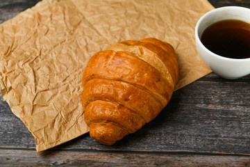 coffee with a croissant. the beginning of the morning. A cup of coffee. fresh french croissant. Coffee cup and fresh baked croissants on a wooden background. View from above.