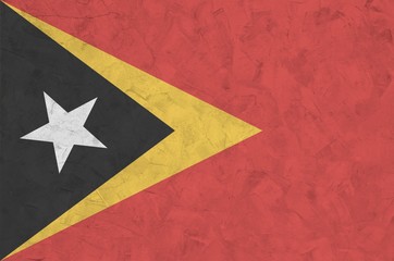 Timor Leste flag depicted in bright paint colors on old relief plastering wall. Textured banner on...