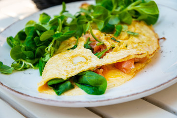 Tasty homemade omelette with fresh salmon served with lettuce on top in white ceramic vintage plate