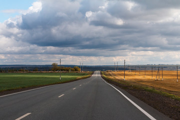 road landscape with dramatic clouds, green and yellow fields, space for text