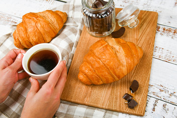 Girl holds a coffee mug. on the background of a croissant. coffee with a croissant. the beginning of the morning. Coffee cup. Top view on woman's hands holding a cup with coffee and fresh french crois