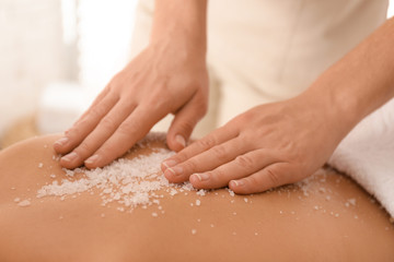 Young woman having body scrubbing procedure with sea salt in spa salon, closeup