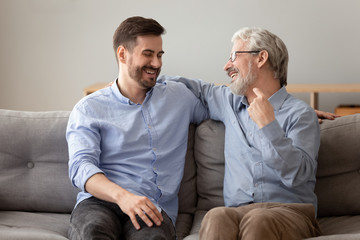 Old father grownup son laughing having fun sitting on sofa