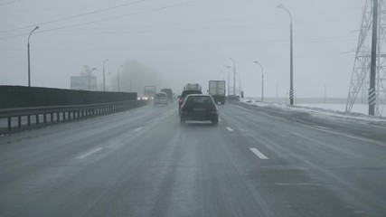 Car goes on the track during blizzard. View from inside cab through windshield glass. Winter daytime snowfall. Bad weather conditions for traffic. Danger for trips. Glassy black ice on the ground road