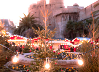 Saint Malo, France - Christmas market with bokeh background and fairy lights decorations next to the famous fort castle.  - obrazy, fototapety, plakaty