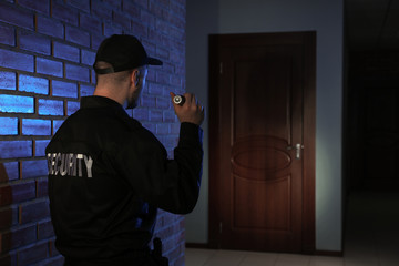 Fototapeta na wymiar Male security guard with flashlight in dark corridor