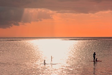 Soft focused sunset scene on coming thunderstorm background. Family silhouettes at sunset on ocean.A father with three children are paddling on two boards.Family supping.