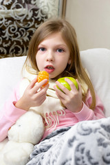 Fototapeta na wymiar A sick little girl takes medication and eats fruit.