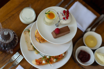  Afternoon tea for two, scones, desserts nad sandwiches, afternoot tower in a restaurant on a wooden table served with tea, jam and butter	