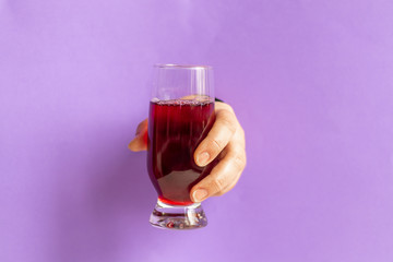 Female hand holds a glass with cherry juice. Inserted into the hole in a sheet of paper. Healthy eating Copy space. 