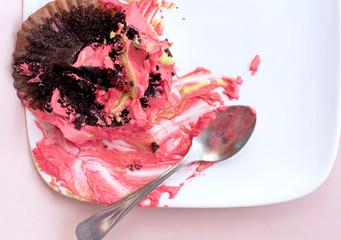 Top view of empty white plate with dirty tasty chocolate cupcake with pink whipped cream and spoon...