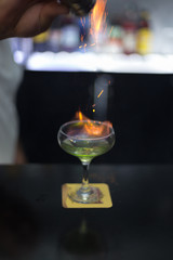 The bartender is lighting a cocktail, a cocktail is lit in a bar