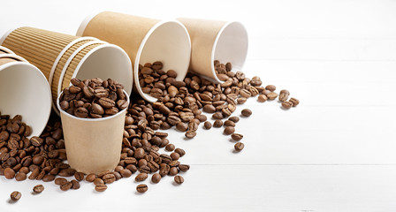 Paper coffee cups with coffee beans on white table