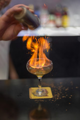 The bartender is lighting a cocktail, a cocktail is lit in a bar