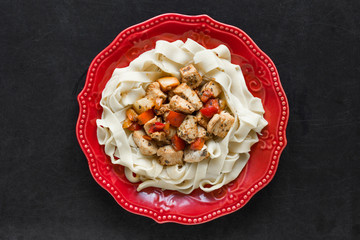 Spaghetti with stew chicken and vegetables on red plate on black background