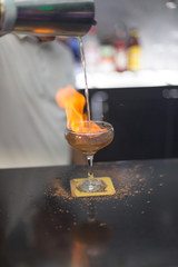 The bartender is lighting a cocktail, a cocktail is lit in a bar