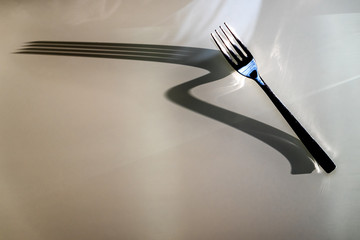 Dinner Fork throws large elongated Shadow on wooden table background. Concept of Shadow and Light