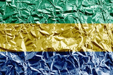 Gabon flag depicted in paint colors on shiny crumpled aluminium foil closeup. Textured banner on...
