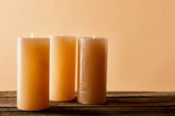 three burning candles on wooden table on beige with copy space