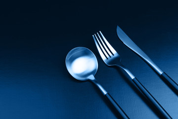 Set of black and gold cutlery on black background.  in trendy blue toning. Main color trend for 2020 year.