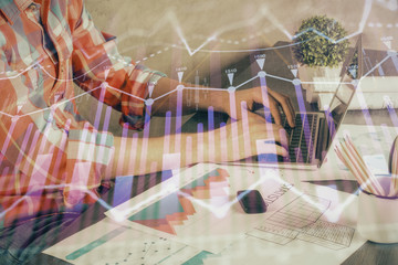 Double exposure of stock graph with businessman typing on computer in office on background. Concept of hard work.