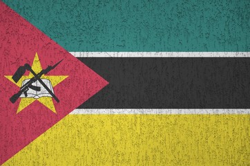 Mozambique flag depicted in bright paint colors on old relief plastering wall. Textured banner on...
