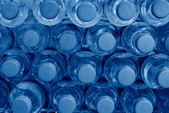 Rows of many transparent plastic bottles with drinking water supply in white refrigerator. Mineral water stack storage in fridge to drink summer day. Pantone color of the year 2020 classic blue toned
