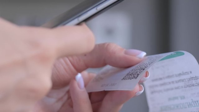 Woman using smartphone and scanning qr code on cash shop receipt paper or bill from store - close up view. Cash back, sales, online shopping, technology, home accountancy, financial concept