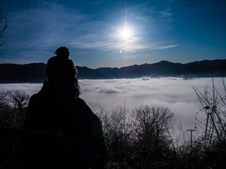 Mujer abrigada y sentada observando Niebla baja  desde una montaña