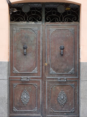 Vintage decorative wooden portal doors with door knockers, handles and a lock.