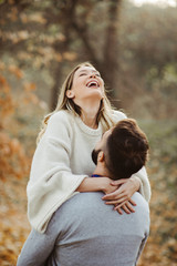 Young cheerful couple having fun in nature during autumn.  Woman being carried by her boyfriend