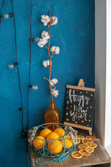 composition of oranges in a Cup on the table with a twig in a vase and the inscription on the Board Happy New Year on the background of a blue wall with a garland