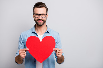 Photo of funny handsome guy holding large red paper heart inviting girlfriend romantic date tender emotions wear specs casual denim clothes isolated grey color background