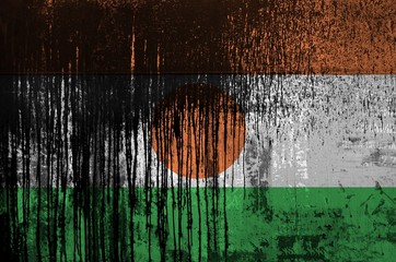 Niger flag depicted in paint colors on old and dirty oil barrel wall closeup. Textured banner on rough background
