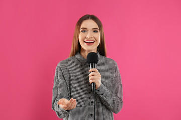 Young female journalist with microphone on pink background