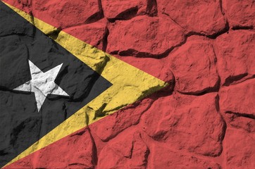 Timor Leste flag depicted in paint colors on old stone wall closeup. Textured banner on rock wall...