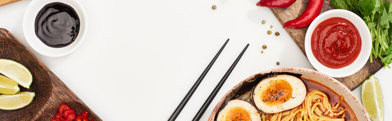 top view of spicy ramen near fresh ingredients and chopsticks on white surface, panoramic shot